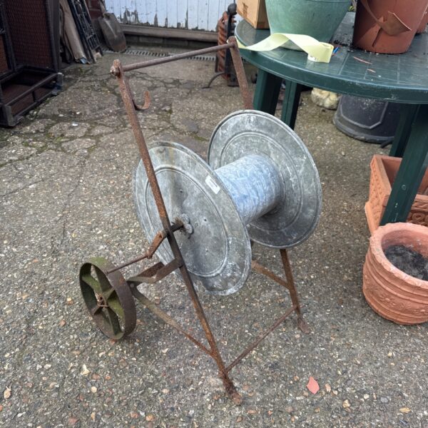 Vintage metal hose reel in a garden setting.