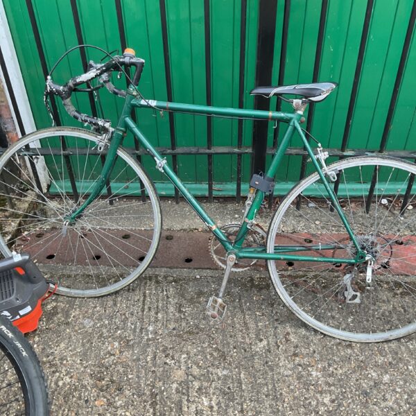 Green vintage racing bicycle leaning against a wall.