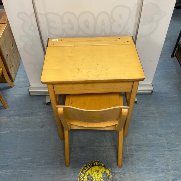 Vintage yellow wooden school desk with chair in a classroom setting.