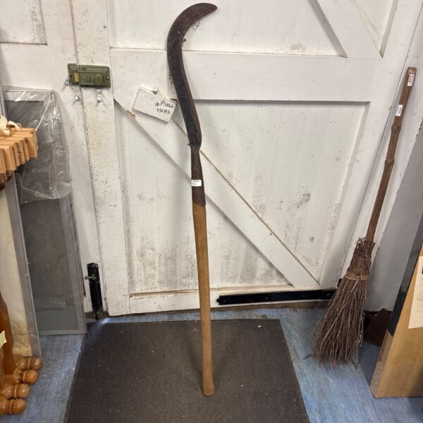 Full view of a vintage scythe with a curved blade and wooden handle.