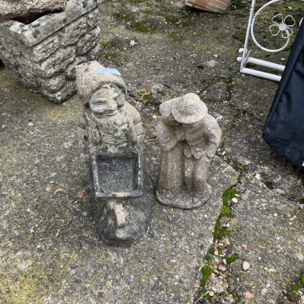 Weathered stone garden ornaments depicting cherubic figures in a garden setting.