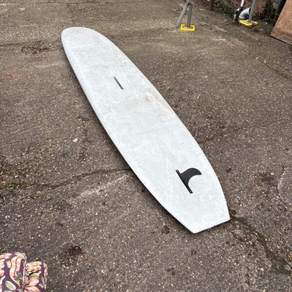 Vintage windsurf board lying on gravel surface.