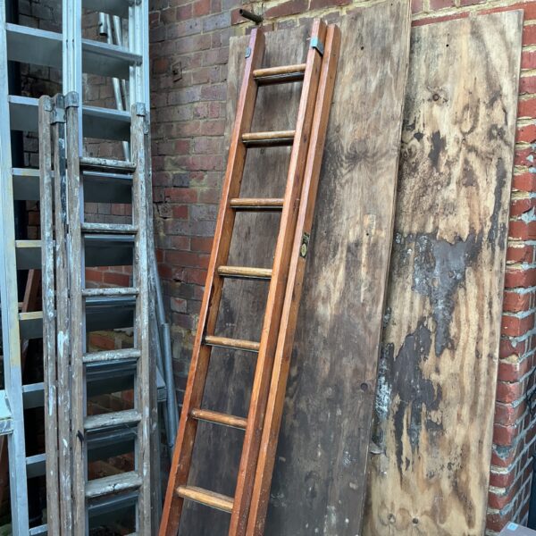Vintage wooden ladder leaning against a brick wall in a garden.