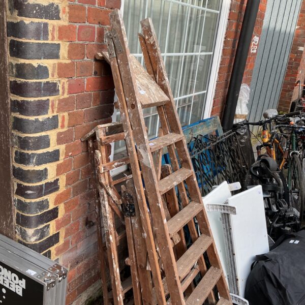 Three vintage wooden step ladders leaning against a wall.