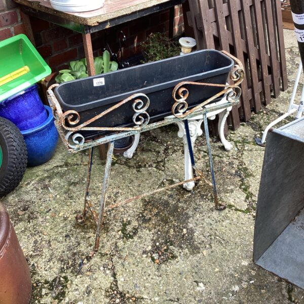 Vintage wrought iron plant stand with decorative scrolls in a garden setting.