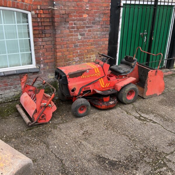 Red Westwood ride on lawnmower with attachments in a garden setting.