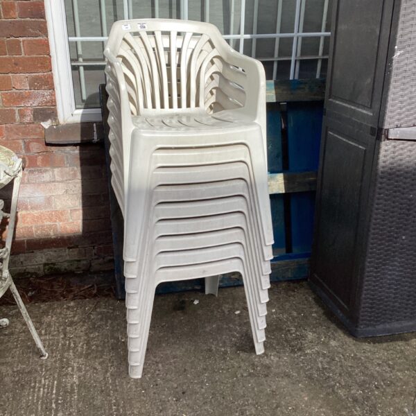 White plastic garden chairs stacked outdoors, ideal for patio seating.