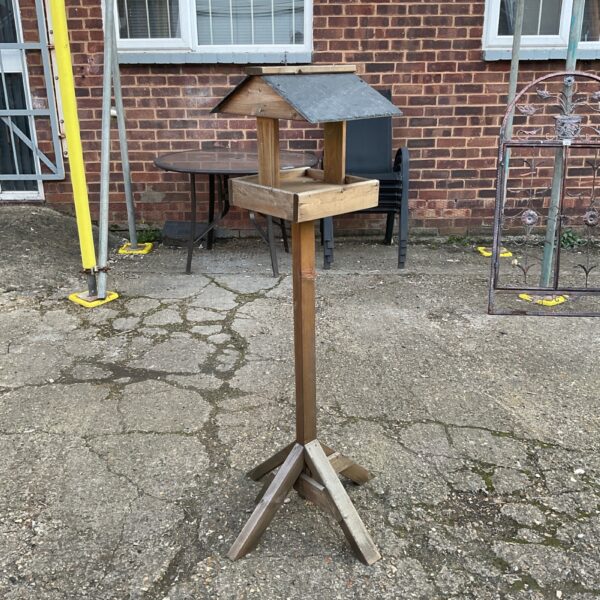 Rustic wooden bird house with slate roof in a garden setting.