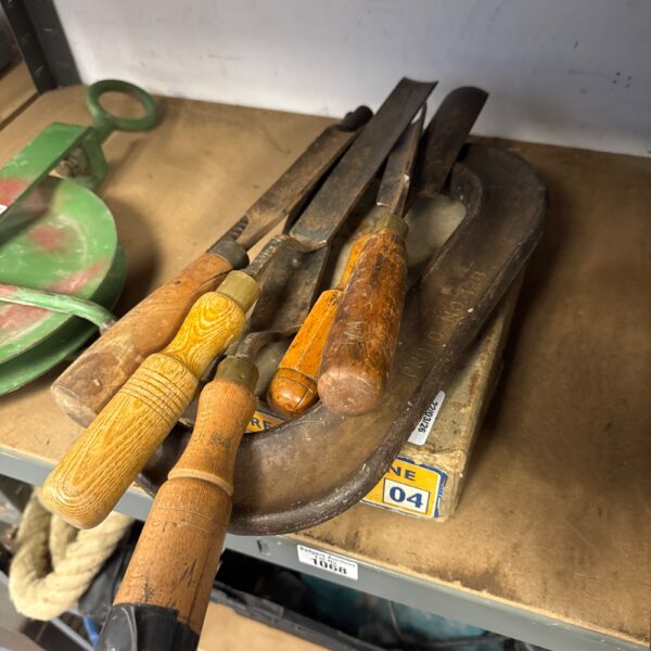 Vintage woodworking chisels, clamp and plane in a workshop setting.