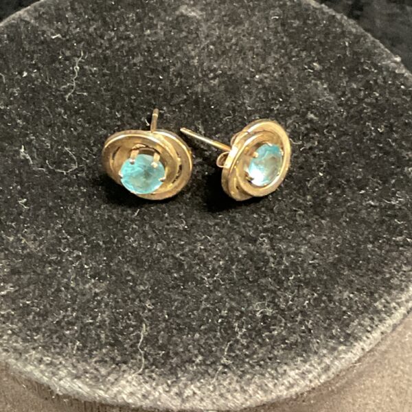 Close-up of 9ct gold topaz stud earrings on a dark background.