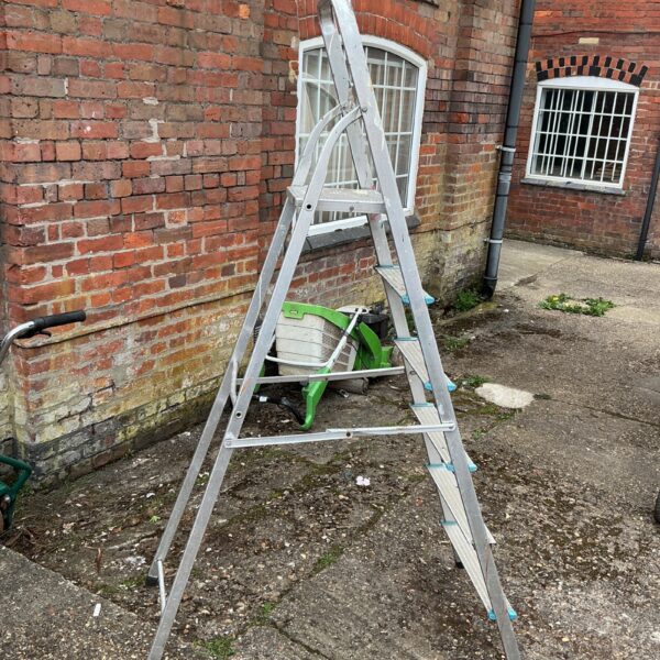 Silver aluminium step ladder leaning against a brick wall.