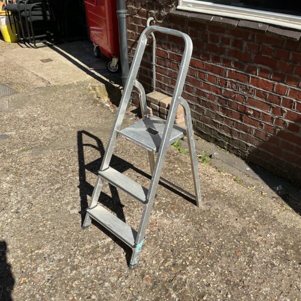 Silver aluminium three-step ladder leaning against a wall.