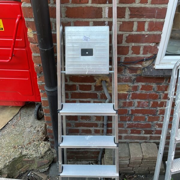 Side view of a three-step aluminium ladder against a brick wall.