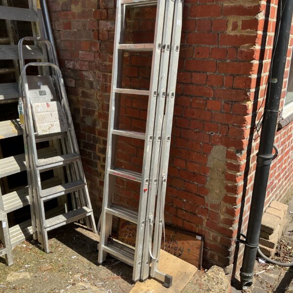 Silver aluminium triple extending ladder leaning against a wall.