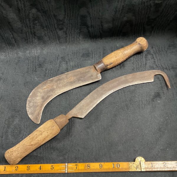 Pair of antique billhooks with curved blades and wooden handles.