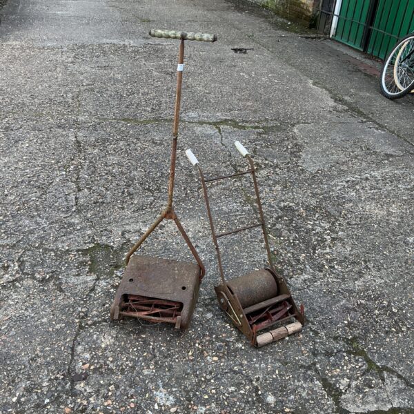 Pair of antique children’s lawn mowers in a garden setting.