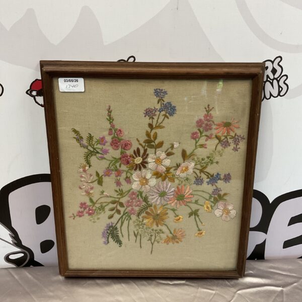 Antique floral embroidery with vibrant stitched flowers in a wooden frame.