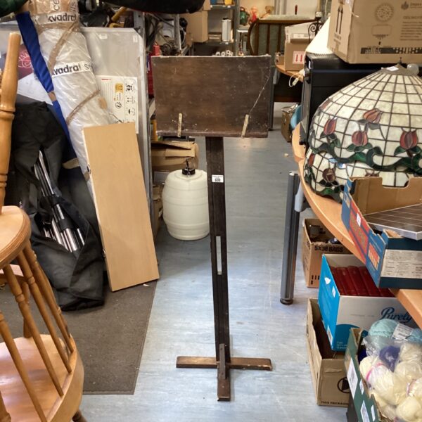 Antique wooden lectern with tripod base in a cluttered room.