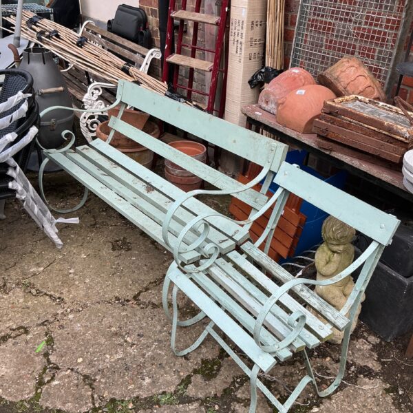 Antique wrought iron garden bench with scrolling details in a garden setting.