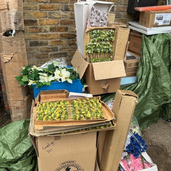 Large bulk lot of colourful artificial flowers in cardboard boxes.