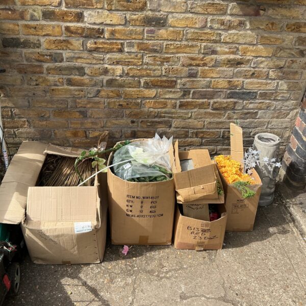 Bulk lot of colourful artificial flowers in cardboard boxes.