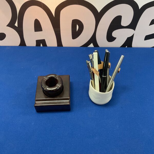 Vintage Bakelite inkwell with a selection of pens on a dark surface.