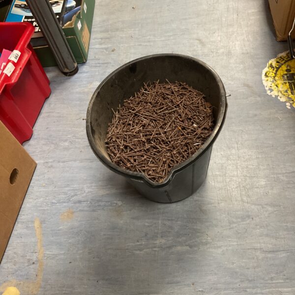 Black bucket filled with a large quantity of small metal nails.
