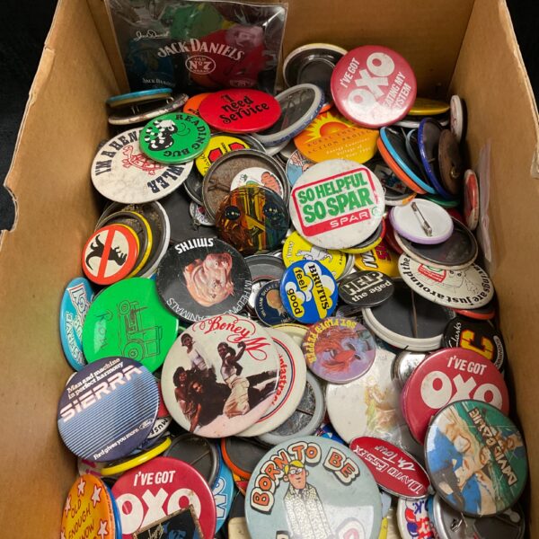 Large collection of assorted button pin badges in a cardboard box.