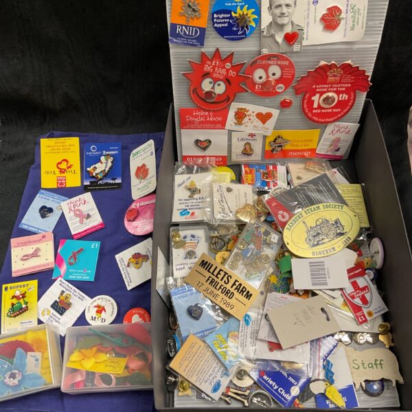 Large assortment of colourful charity badges, including Red Nose Day pins.