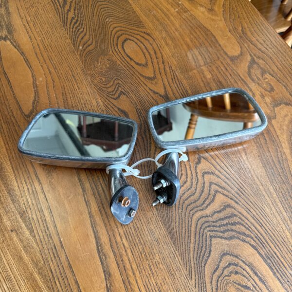 Vintage chrome car wing mirrors on a wooden surface.