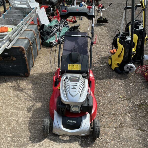 Side view of a red Cobra petrol lawn mower in used condition.