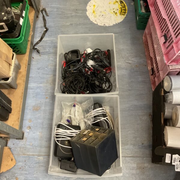 Mixed lot of electronic accessories and power supplies in a plastic container.