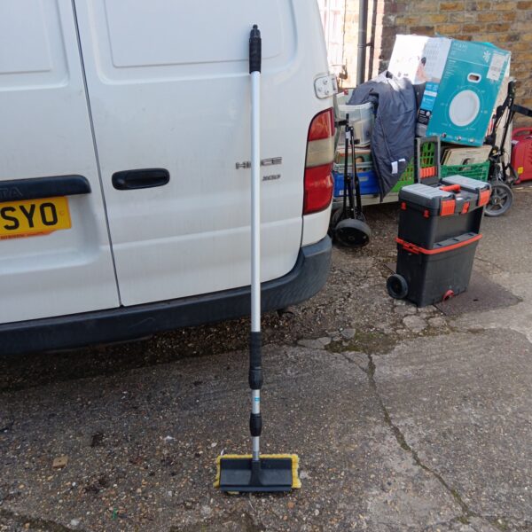 Hug Flight extending cleaning brush leaning against a van.