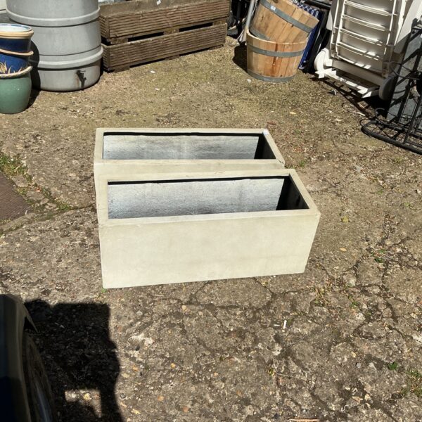 Two long rectangular fibreglass planters in a garden setting.