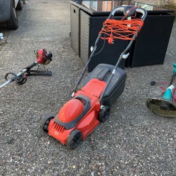 Side view of a used Flymo electric lawn mower in a garden setting.