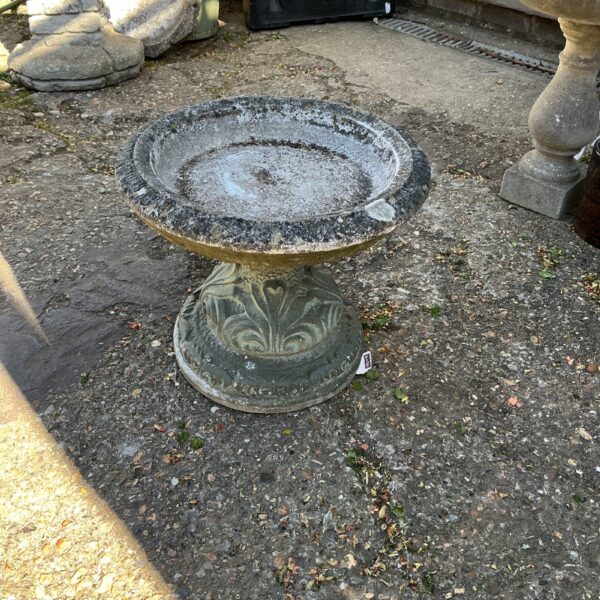 Weathered stone garden bird bath with fluted pedestal.