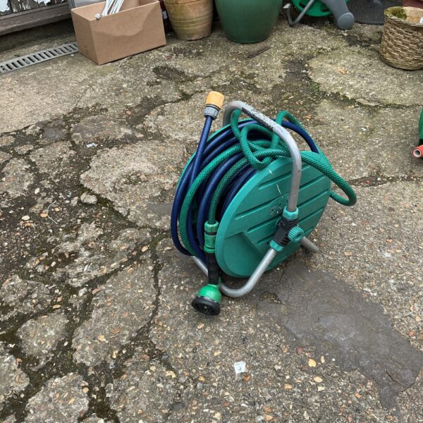 Green garden hose reel with attached hose in a garden setting.