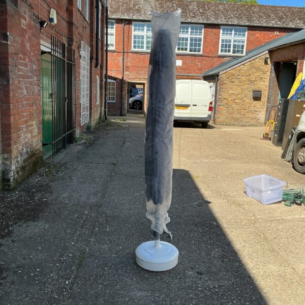 Dark grey garden parasol with a white base standing outdoors.