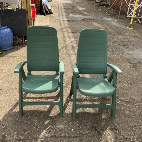 Two green plastic garden reclining chairs on a patio.