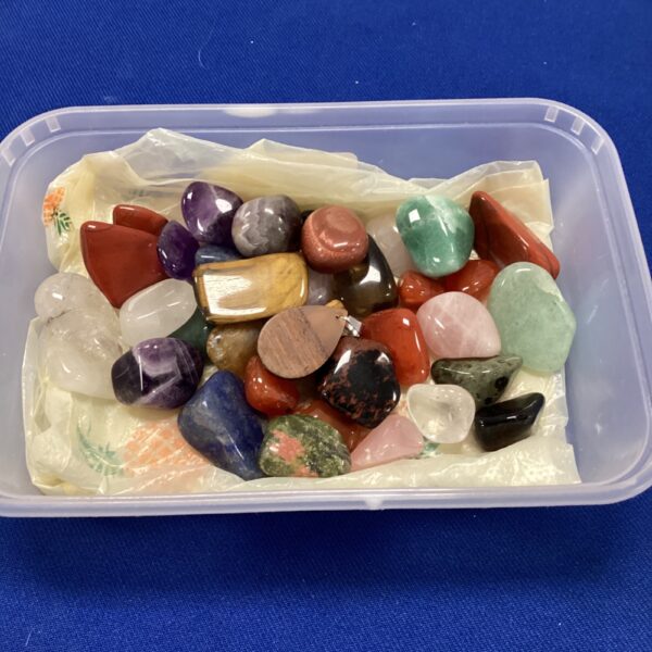 Colourful tumbled gemstone collection in a clear container.