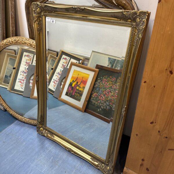Large gilt framed bevelled mirror with ornate detailing.