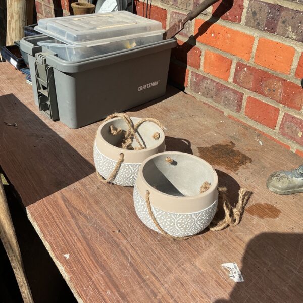 Two ceramic hanging garden pots with rope hangers.