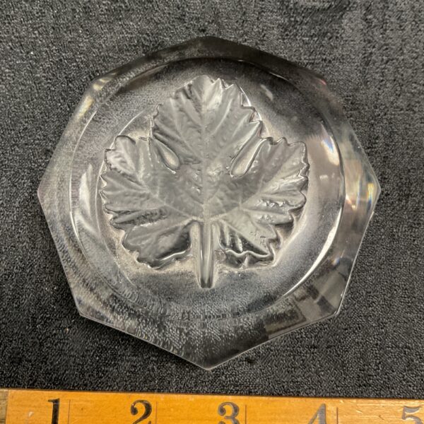 Clear glass Lalique maple leaf paperweight on a dark surface.