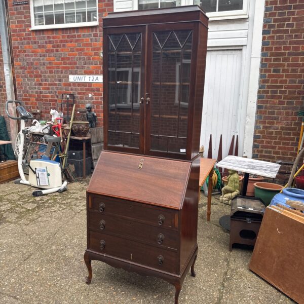 Antique mahogany writing bureau bookcase in a rustic setting.