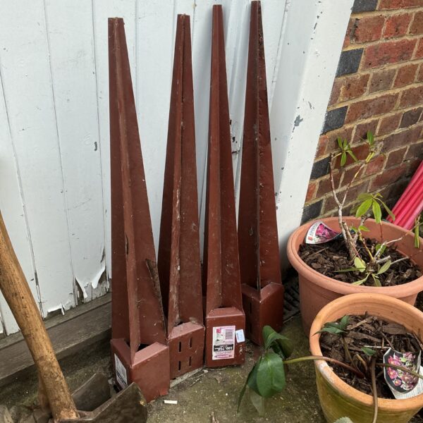 Four metal fence post holders in a garden setting.