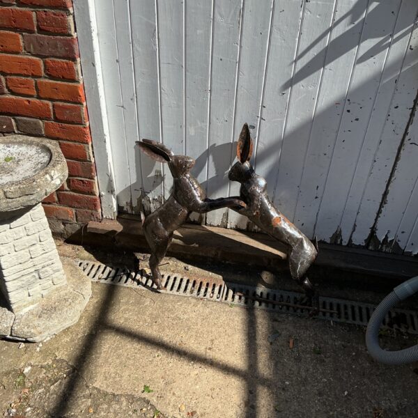 Rustic metal fighting hares garden ornament in outdoor setting.