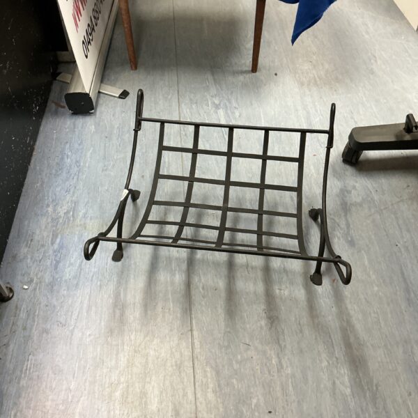 Dark metal log rack for firewood storage near a fireplace.