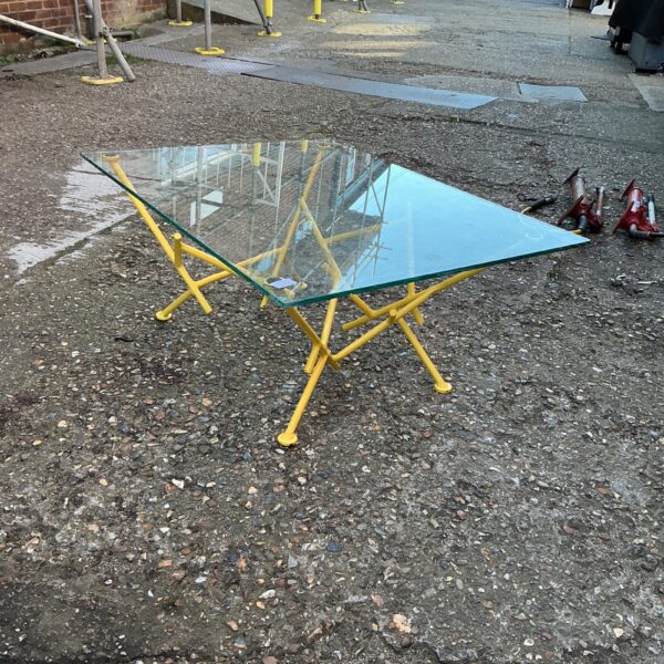 Modern coffee table with clear glass top and yellow metal legs.