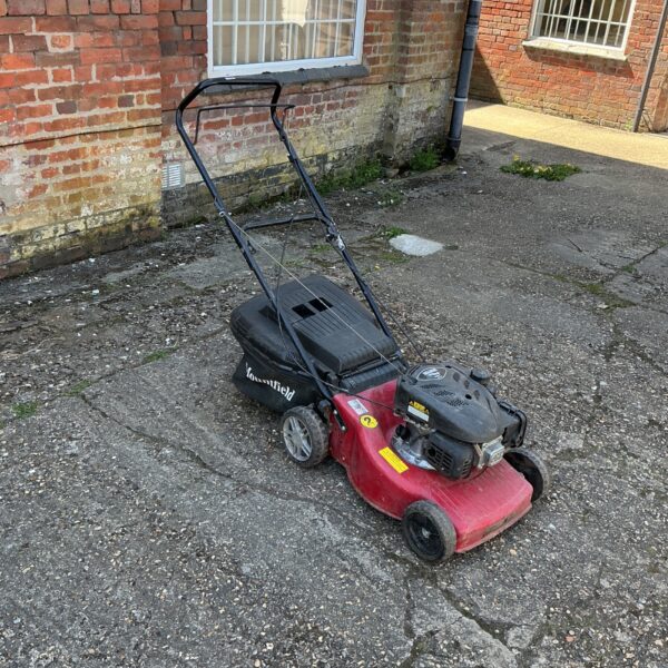 Red Mountfield petrol lawnmower in a garden setting.