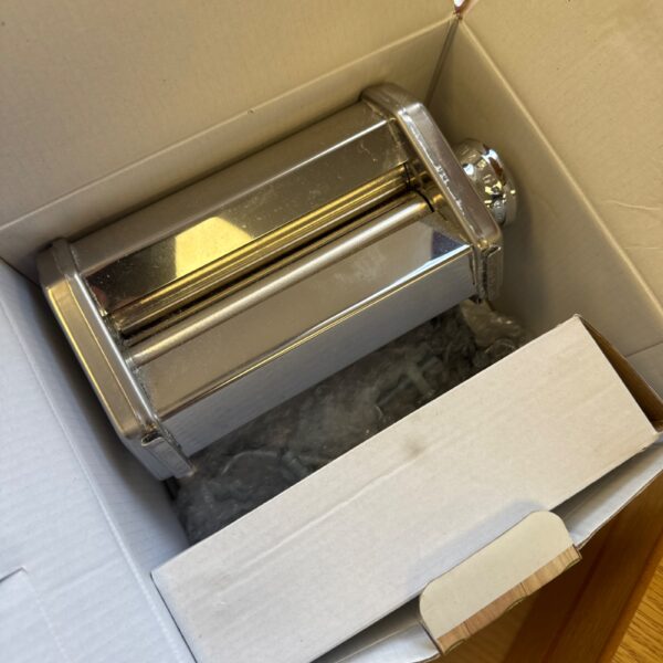 Stainless steel pasta making machine inside its original packaging.